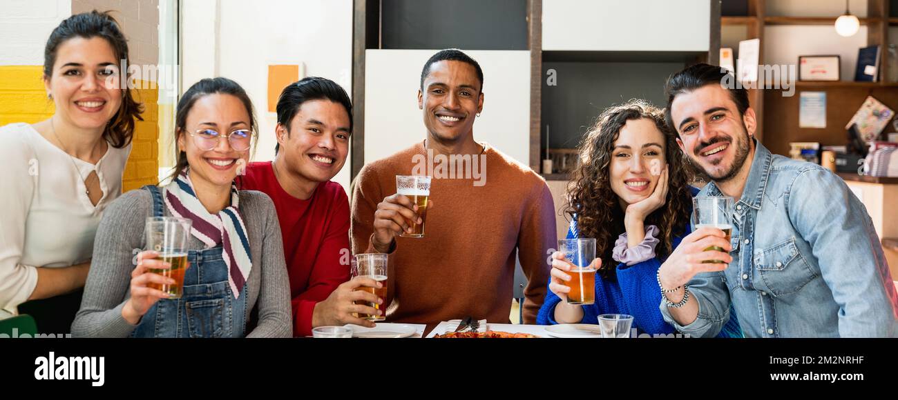 Bannière horizontale ou en-tête portrait d'un groupe multiethnique de jeunes amis assis à table manger de la pizza et boire de la bière posant à la caméra avec heureux Banque D'Images