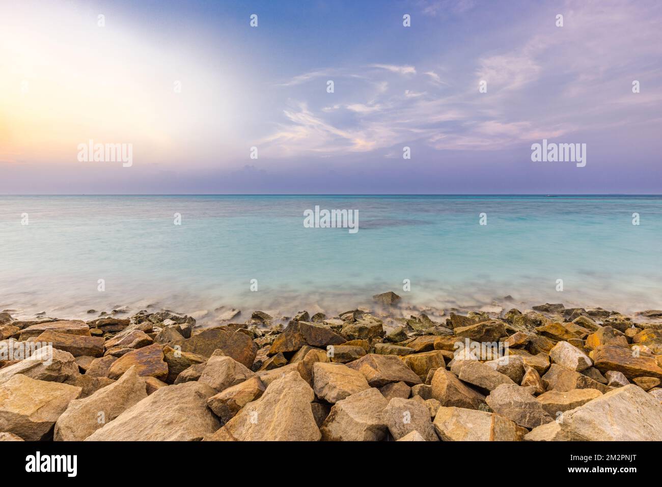 Vue sur l'île tropicale avec beau coucher de soleil sur les rochers verts sur un brise-vague. Rochers sur une rive exotique sous un ciel et un horizon colorés. Mer exotique Banque D'Images