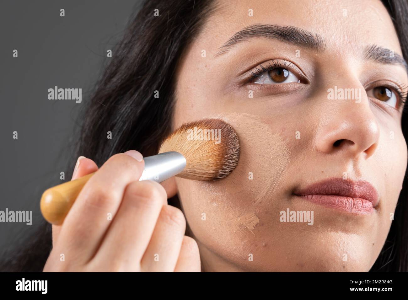 Image rapprochée d'une femme attrayante appliquant une fondation tonale liquide. Tenir et utiliser la brosse pour faire son propre maquillage. Idée de concept de soins de la peau. Banque D'Images