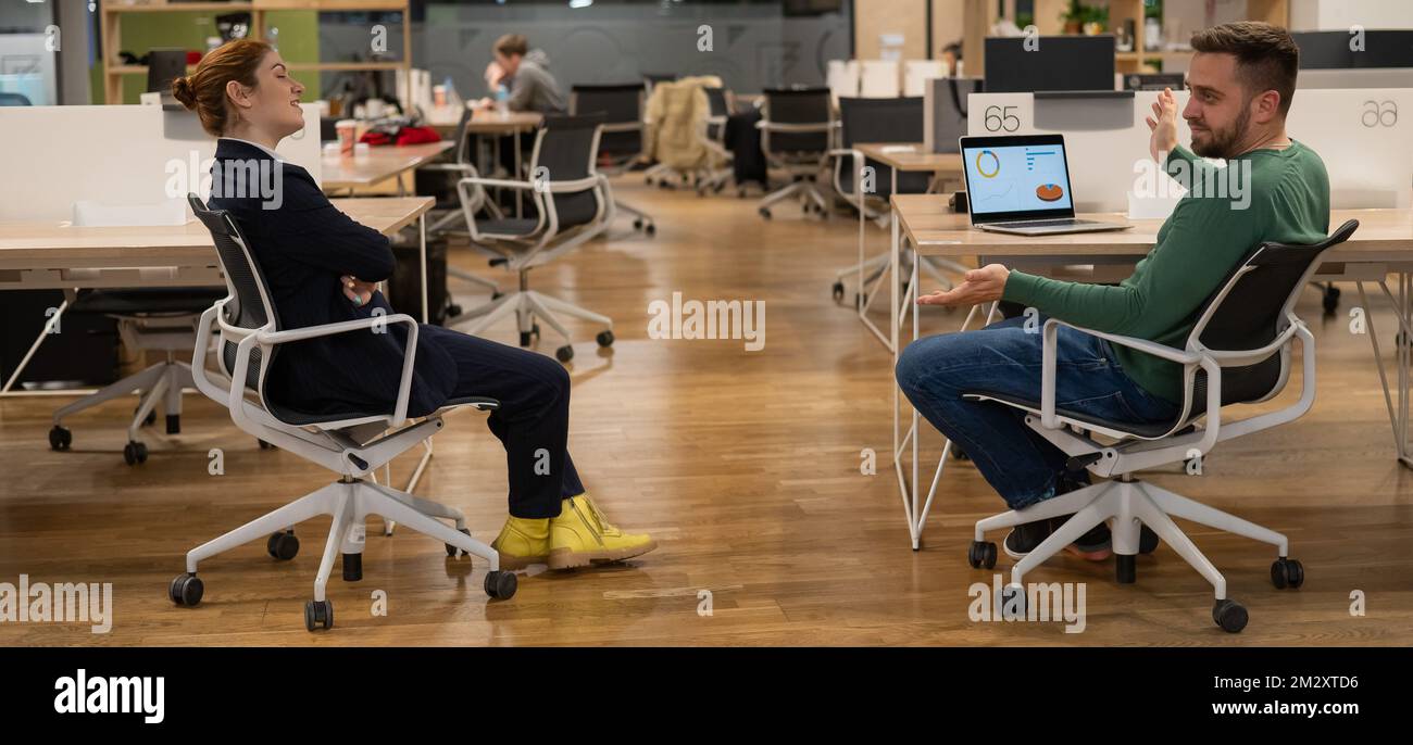 REDHEAD la femme caucasienne et l'homme barbu sont assis sur des chaises dans un bureau à espace ouvert. Banque D'Images REDHEAD la femme caucasienne et l'homme barbu sont assis sur des chaises dans un bureau à espace ouvert. Banque D'Images
