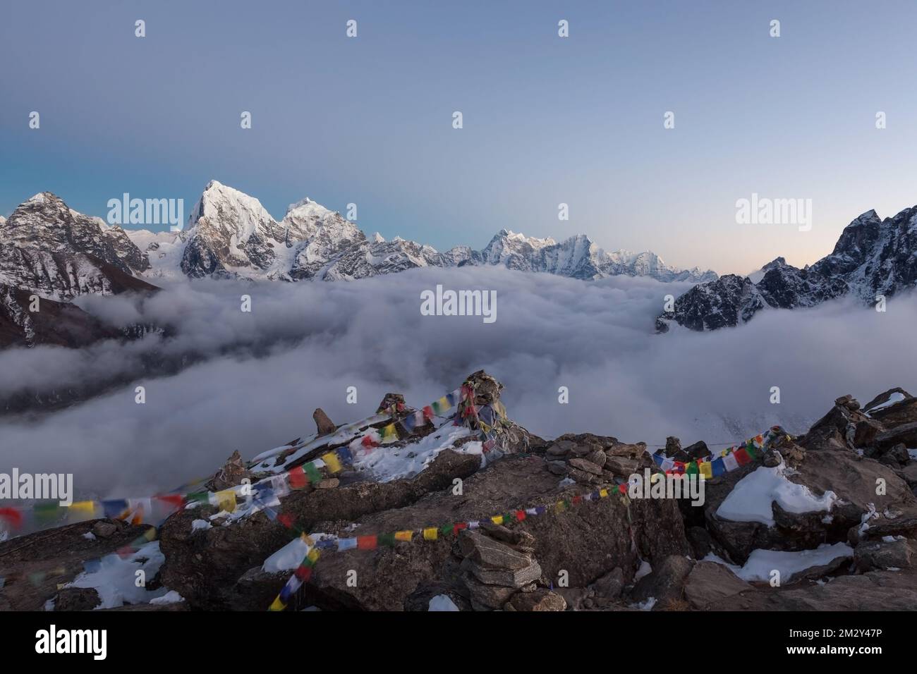 Vue sur le mont Cholatse depuis Gokyo RI. Pittoresque vallée de montagne remplie de nuages mauriques au coucher du soleil. Et drapeaux bouddhistes tibétains à l'avant-plan. Sa Banque D'Images