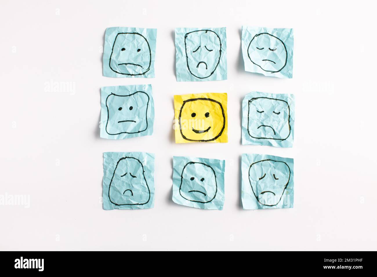 Un triste visage regardant des visages souriants de loin. Visages heureux et tristes dessinés sur des autocollants bleus. Concepts d'exclusion, de différence, de jalousie. Pho de haute qualité Banque D'Images