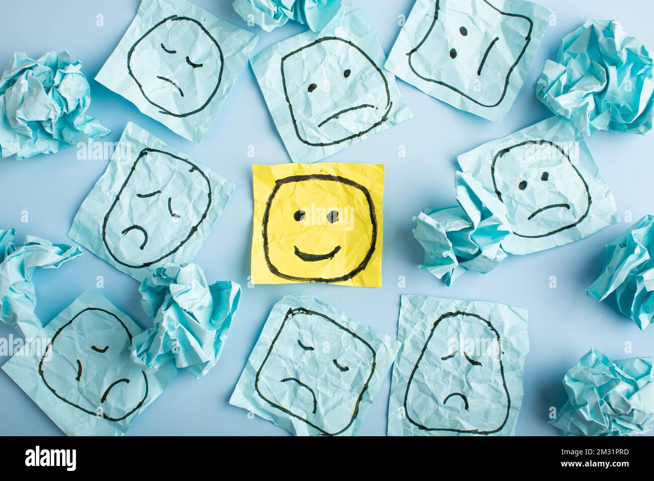 Un triste visage regardant des visages souriants de loin. Visages heureux et tristes dessinés sur des autocollants bleus. Concepts d'exclusion, de différence, de jalousie. Pho de haute qualité Banque D'Images