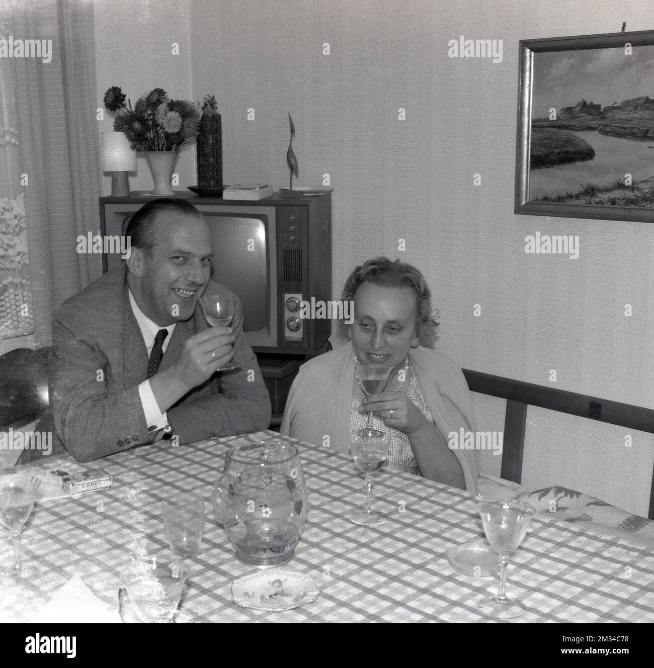 Années 1960, historique, un homme et une dame assis à une table sur une salle de devant dégustant un verre de vin, Angleterre, Royaume-Uni. Un téléviseur de l'époque peut être vu dans le coin. Banque D'Images Années 1960, historique, un homme et une dame assis à une table sur une salle de devant dégustant un verre de vin, Angleterre, Royaume-Uni. Un téléviseur de l'époque peut être vu dans le coin. Banque D'Images