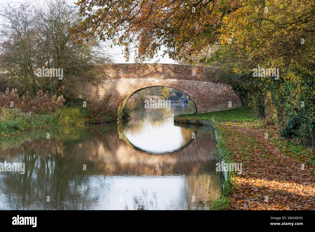 Watford, Northamptonshire, Royaume-Uni : à la fin de l'automne, un pont de canal typique traverse le canal de Grand Union, le reflet de son arche faisant un cercle. Banque D'Images