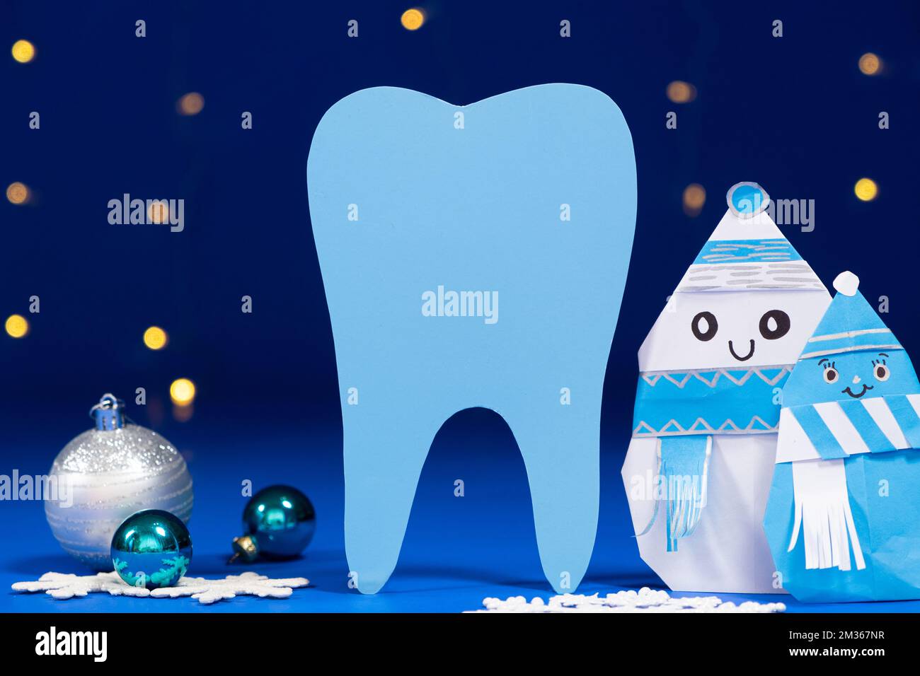 Dentisterie de Noël - grosse dent, bonhomme de neige et boules sur fond bleu, guirlande de bokeh. Banque D'Images