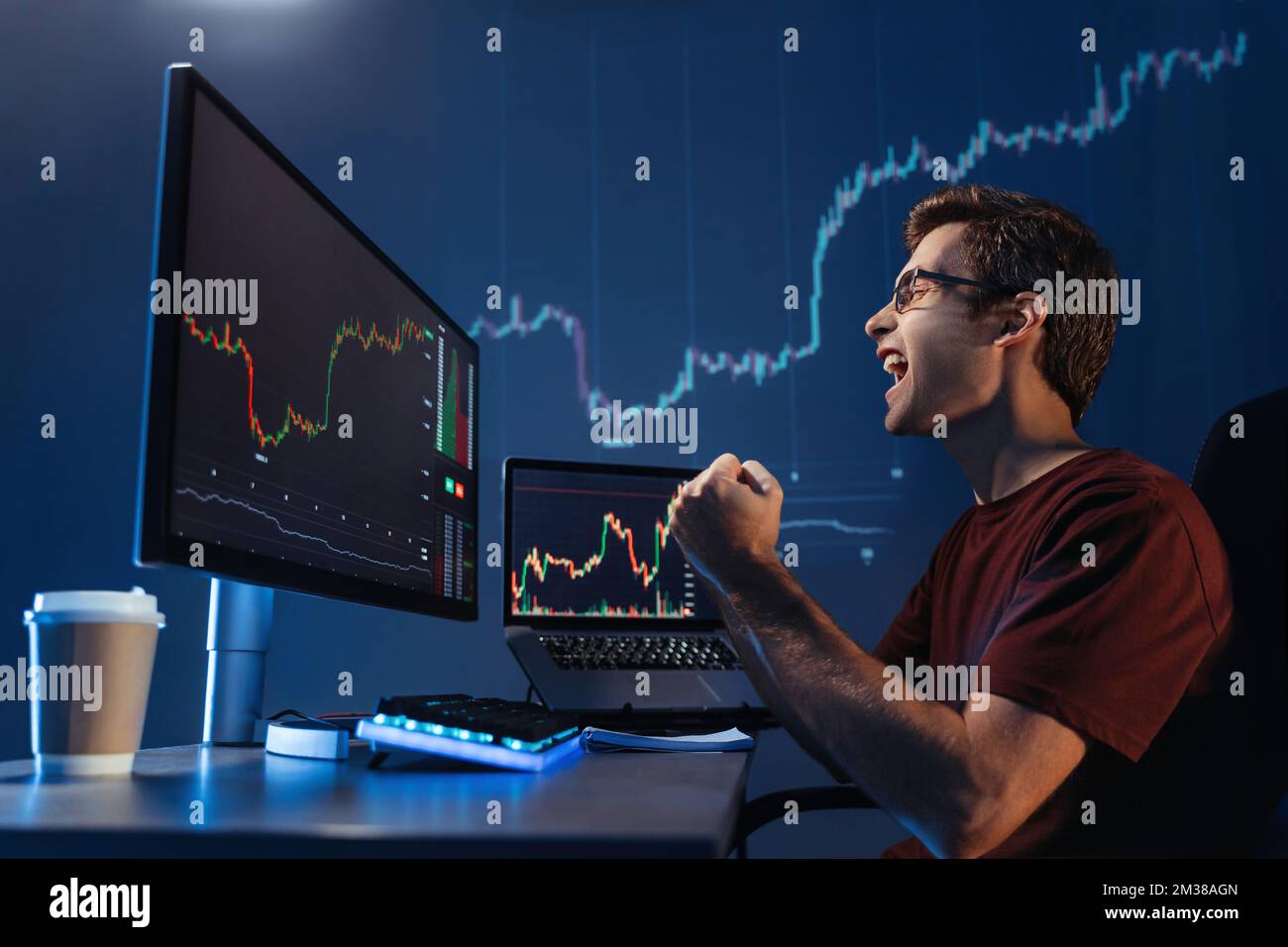 Vue de côté de crypto Trader mâle faisant oui geste criant avec triomphe. Homme sorti regardant l'écran avec le tableau numérique de chandelier de la bourse de crypto-monnaie et du marché d'investissement Banque D'Images