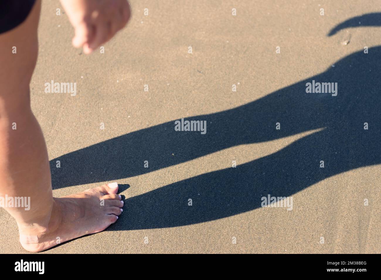 silhouette sur une plage de sable brun uni d'une jambe de femme Banque D'Images