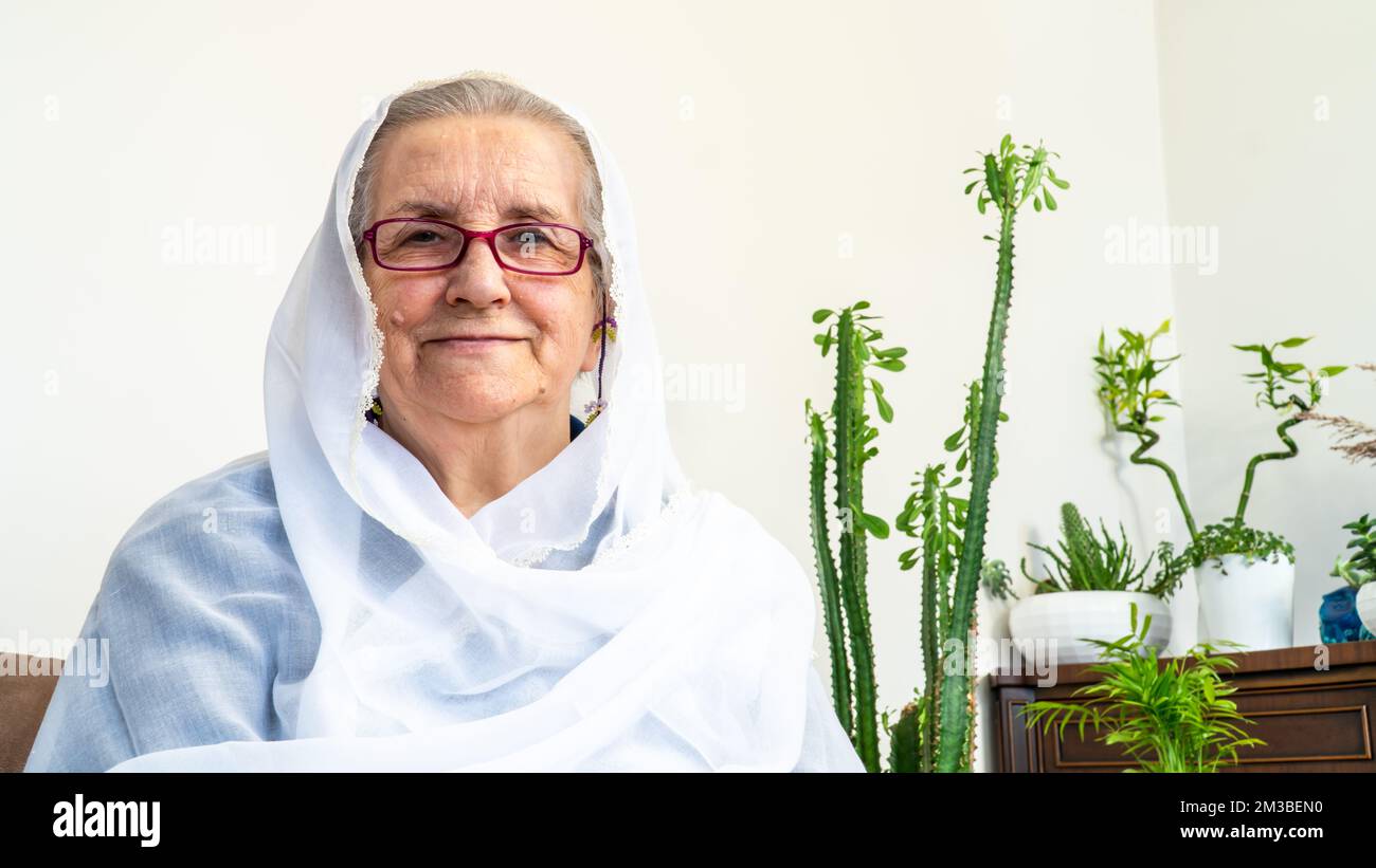 Portrait d'une vieille femme musulmane des années 80 portant le hijab blanc assis à la maison pendant le jeûne pendant le mois du Ramadan. Banque D'Images