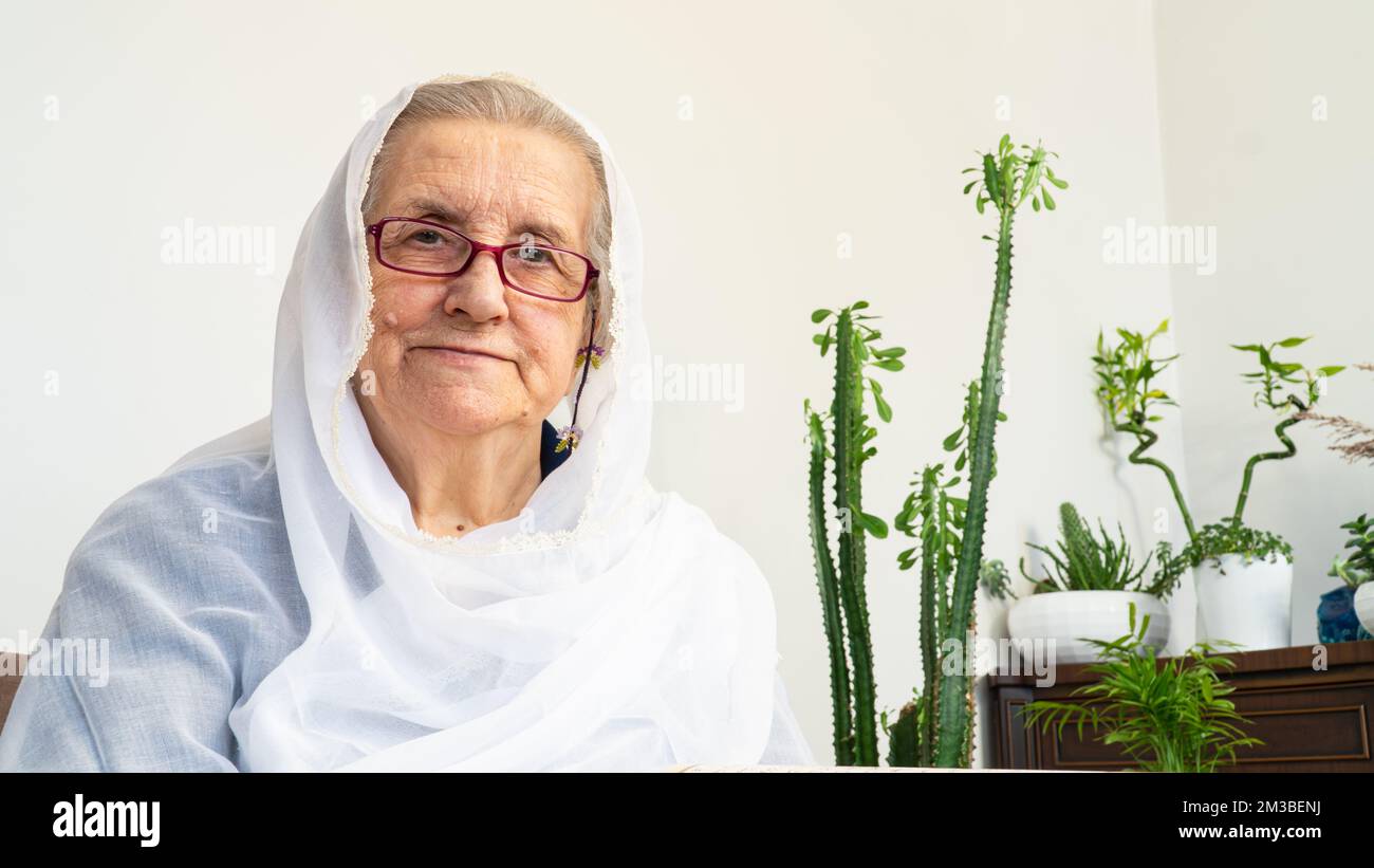 Portrait d'une vieille femme musulmane des années 80 portant le hijab blanc assis à la maison pendant le jeûne pendant le mois du Ramadan. Banque D'Images