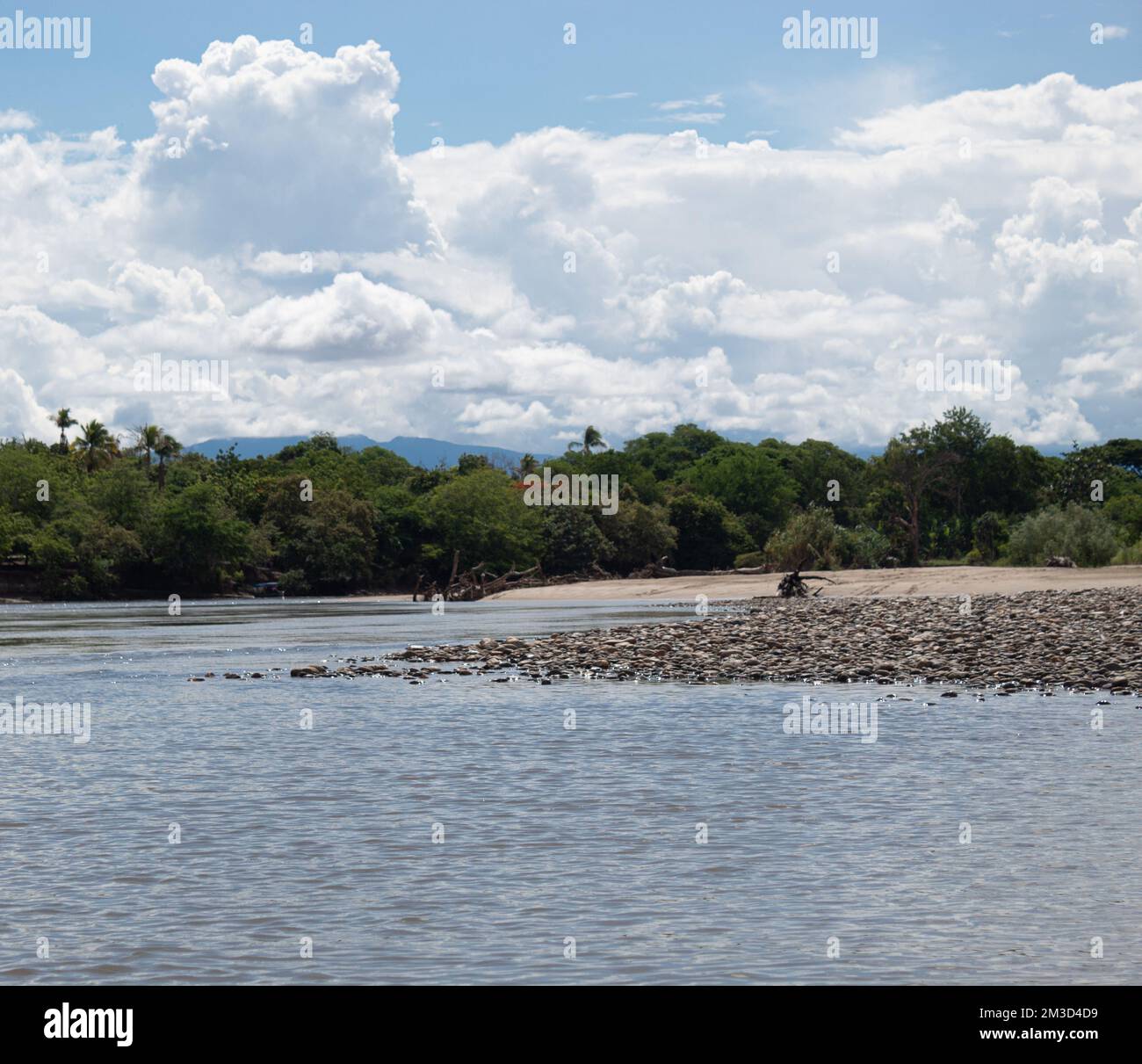 Rivière Magdalena en journée ensoleillée avec pierres, bancs de sable, arbres et buissons verts, nuages et ciel bleu à l'arrière-plan près de la ville de l'AIPE, Huila Colombie Banque D'Images