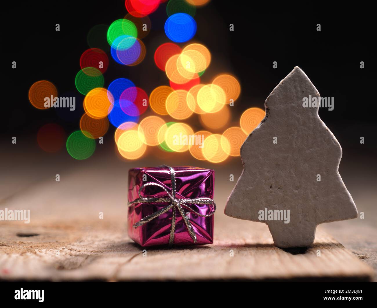 Gros plan d'une boîte cadeau rose avec un arbre en bois sur un fond coloré de lumières de Noël Banque D'Images