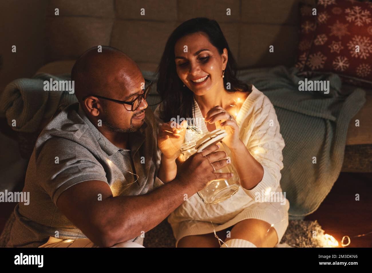 Heureux couple interracial célébrant le nouvel an à la maison ensemble, assis près de l'arbre de Noël Banque D'Images