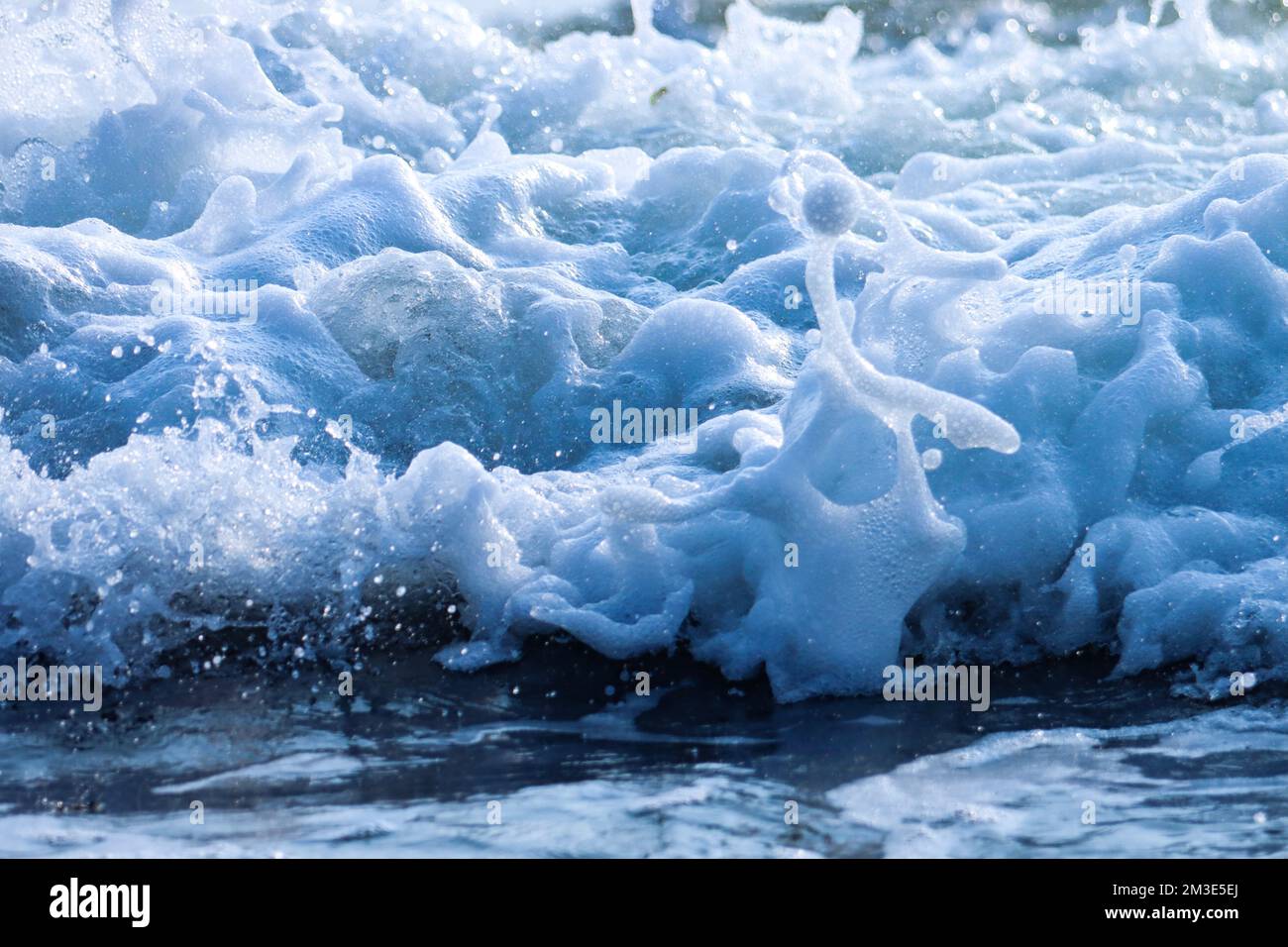 Vagues de mer mousseuse blanche se brisant, barbotant sur la plage. Banque D'Images