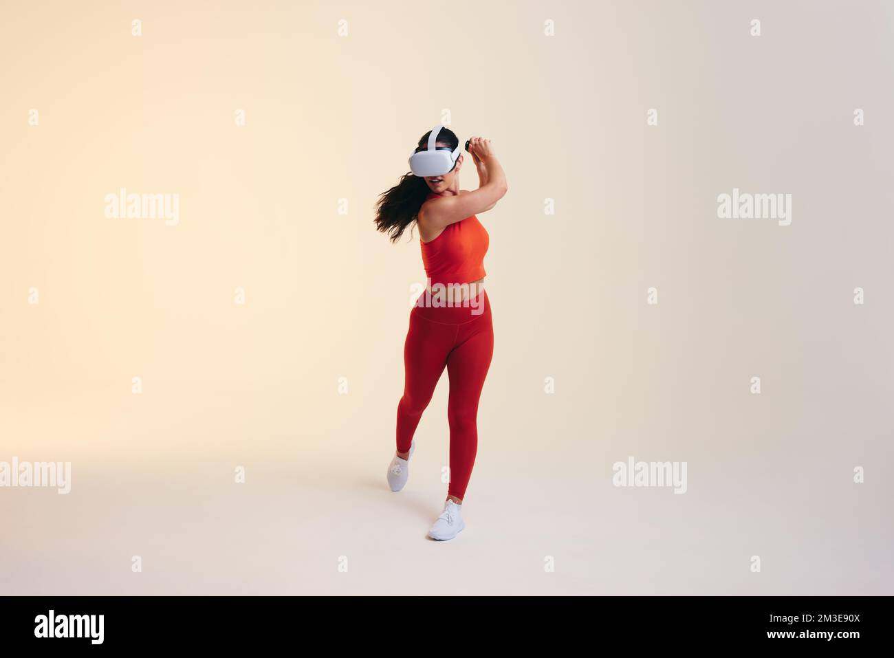 Jeune femme sportive jouant au tennis en réalité virtuelle. Jeune femme sportive balançant une batte de tennis virtuelle à l'aide de contrôleurs de jeu. Port de Sportswoman Banque D'Images