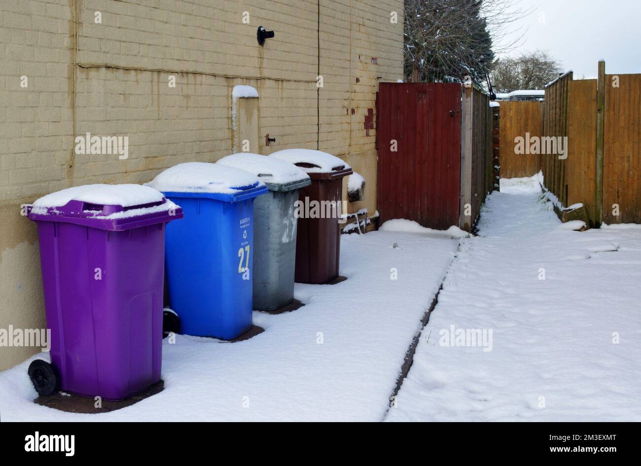 Une rangée de bacs de recyclage de conseil dans différentes couleurs à l'extérieur d'une maison pendant le temps hivernal enneigé Banque D'Images