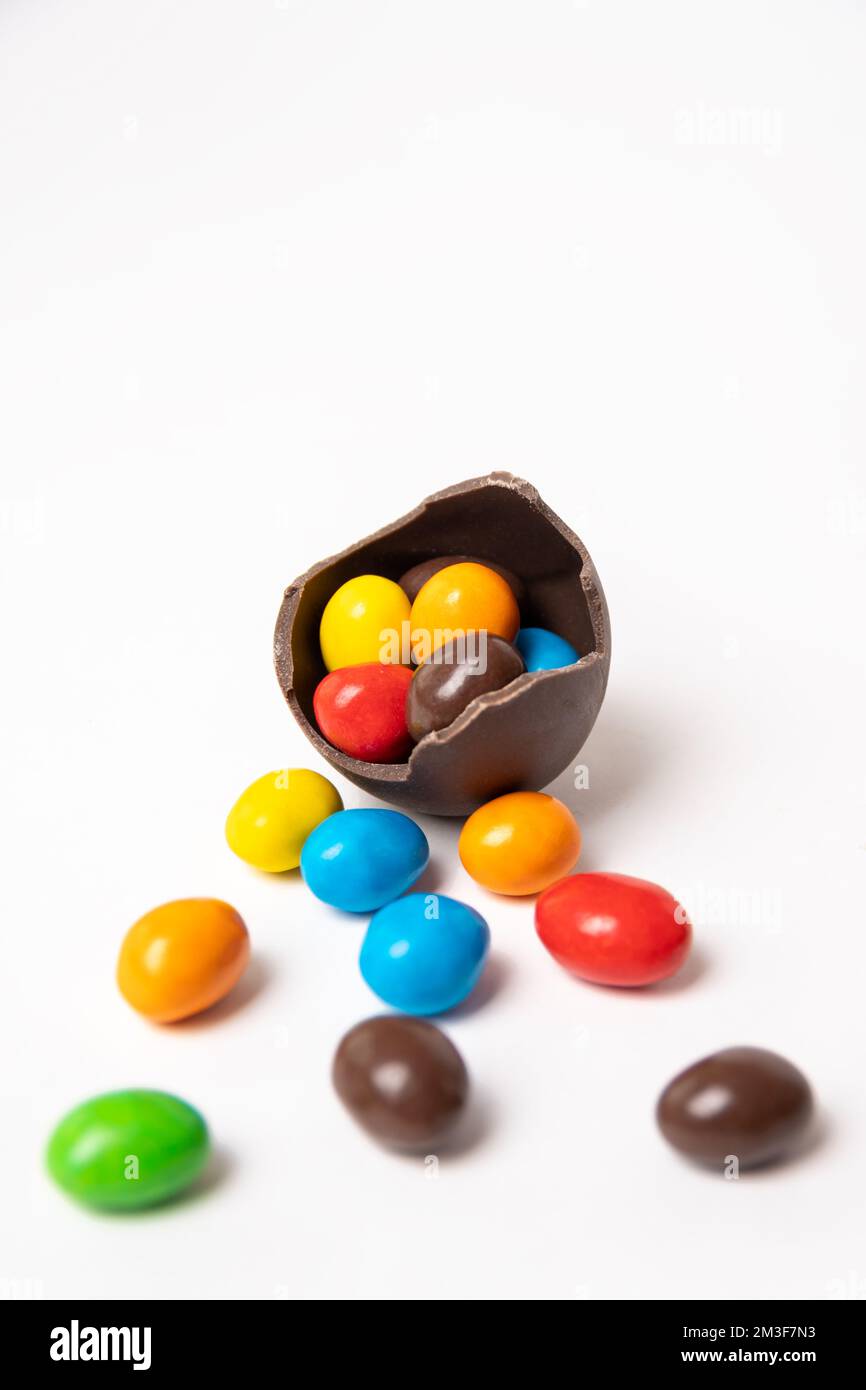 Chocolat craqué oeuf de pâques plein de petites bonbons ronds colorés sur un fond blanc avec des bonbons colorés, espace de copie, cadre vertical. Chocolat t Banque D'Images
