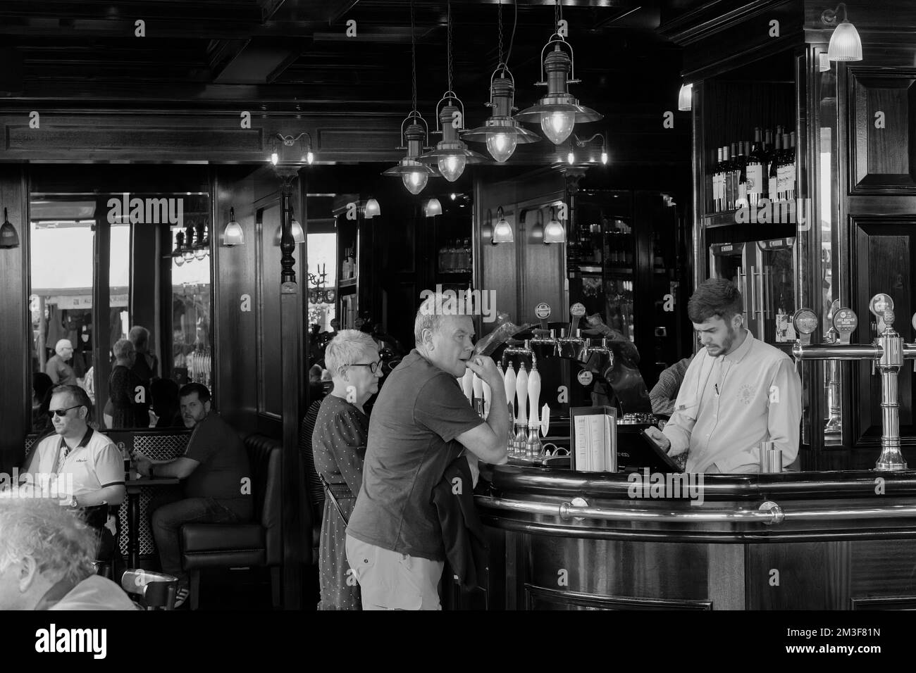 Un barman a tendance à attendre deux clients au bar de la Market Cat public House à York, dans le North Yorkshire, en Angleterre, au Royaume-Uni. Banque D'Images
