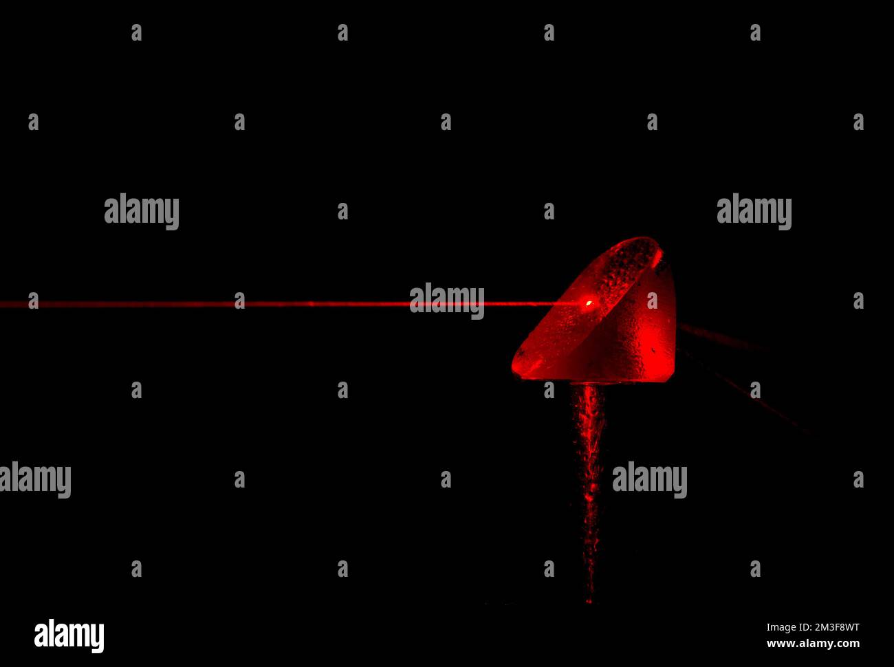 Un faisceau laser rouge frappant un prisme. Le faisceau a été rendu visible par un jet d'eau fin. De l'eau tombe sur le prisme et des traînées d'eau apparaissent dans le faisceau. Banque D'Images