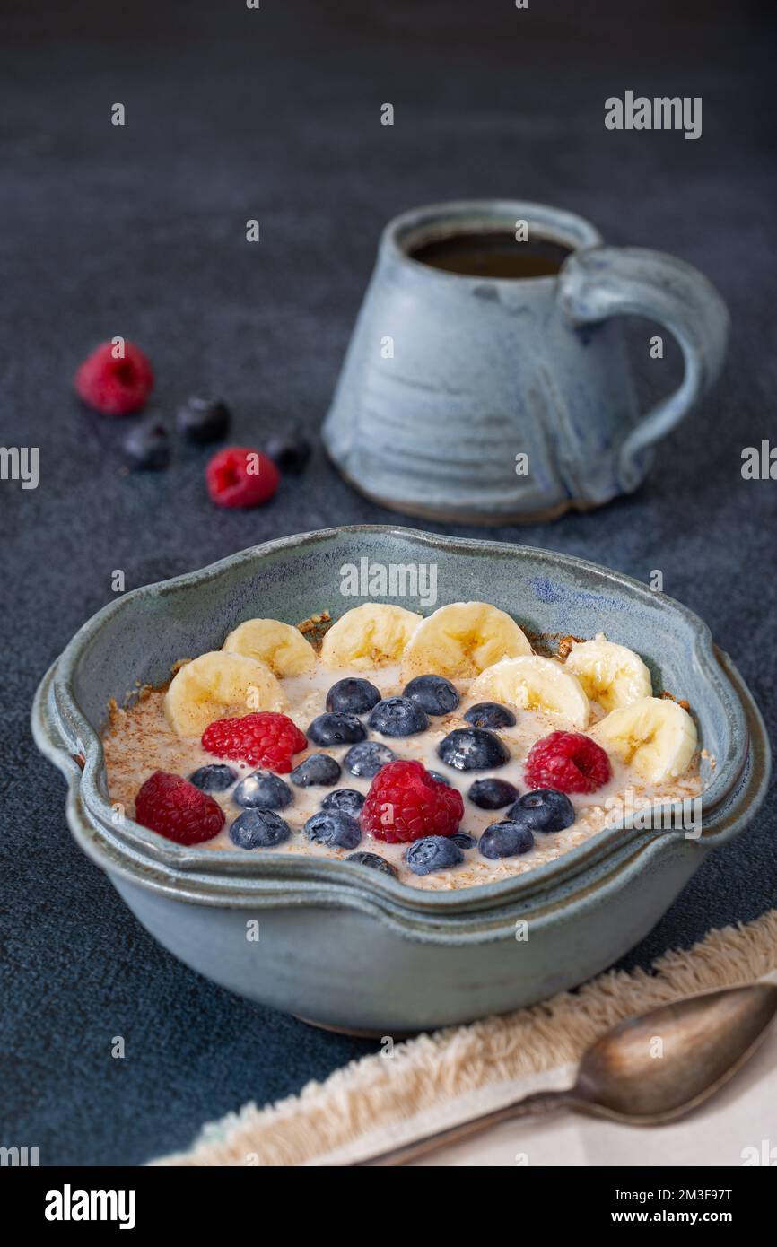 Flocons d'avoine coupés en acier biologique à base de plantes, recouverts de fruits dans un beau bol bleu avec du café dans une tasse assortie; espace de copie Banque D'Images