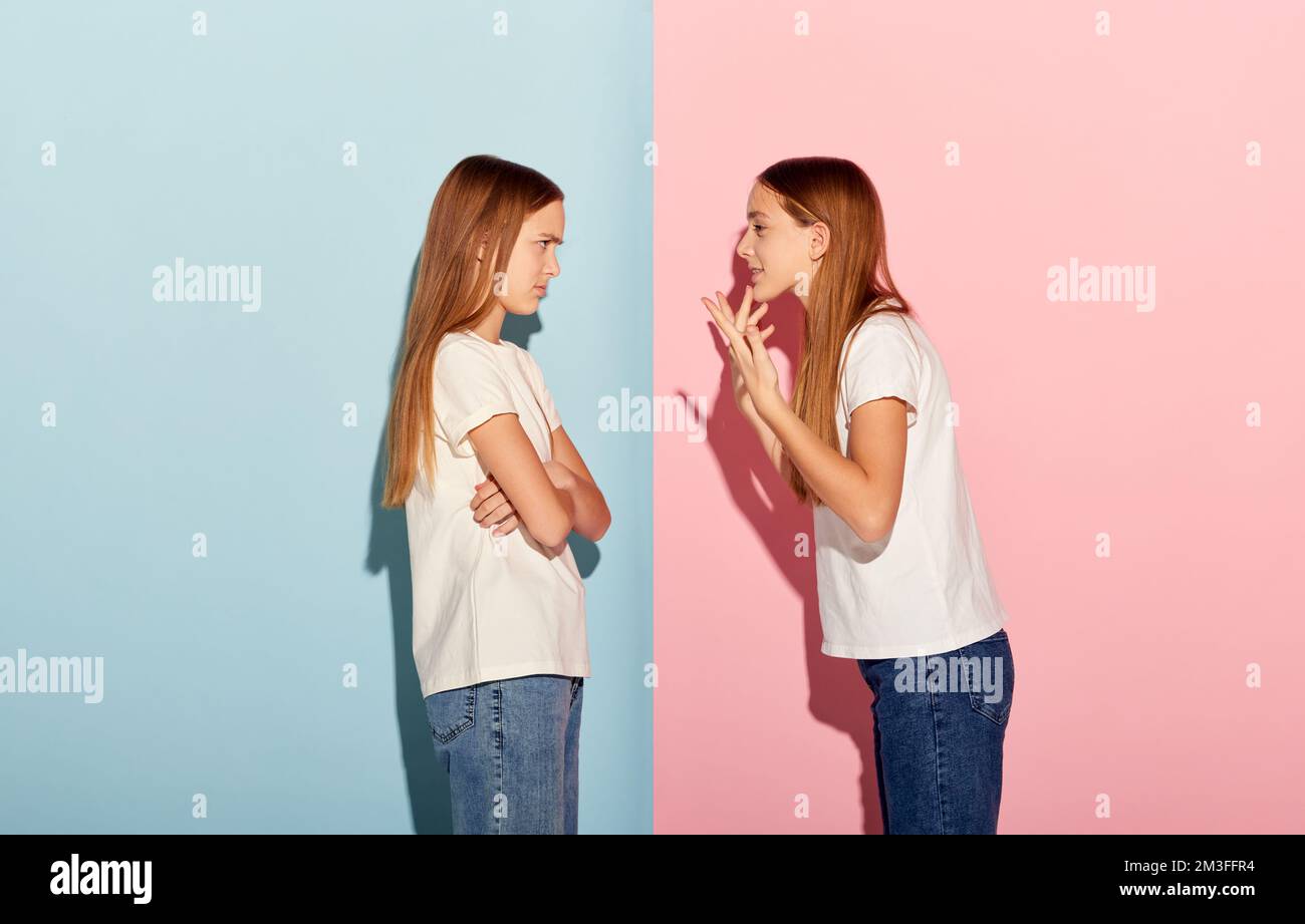 Argumenter. Deux belles filles adolescentes, frères et sœurs en t-shirts et jeans posant isolés sur un arrière-plan duotone rose-bleu. Émotions, famille, plaisir, joie, loisirs Banque D'Images