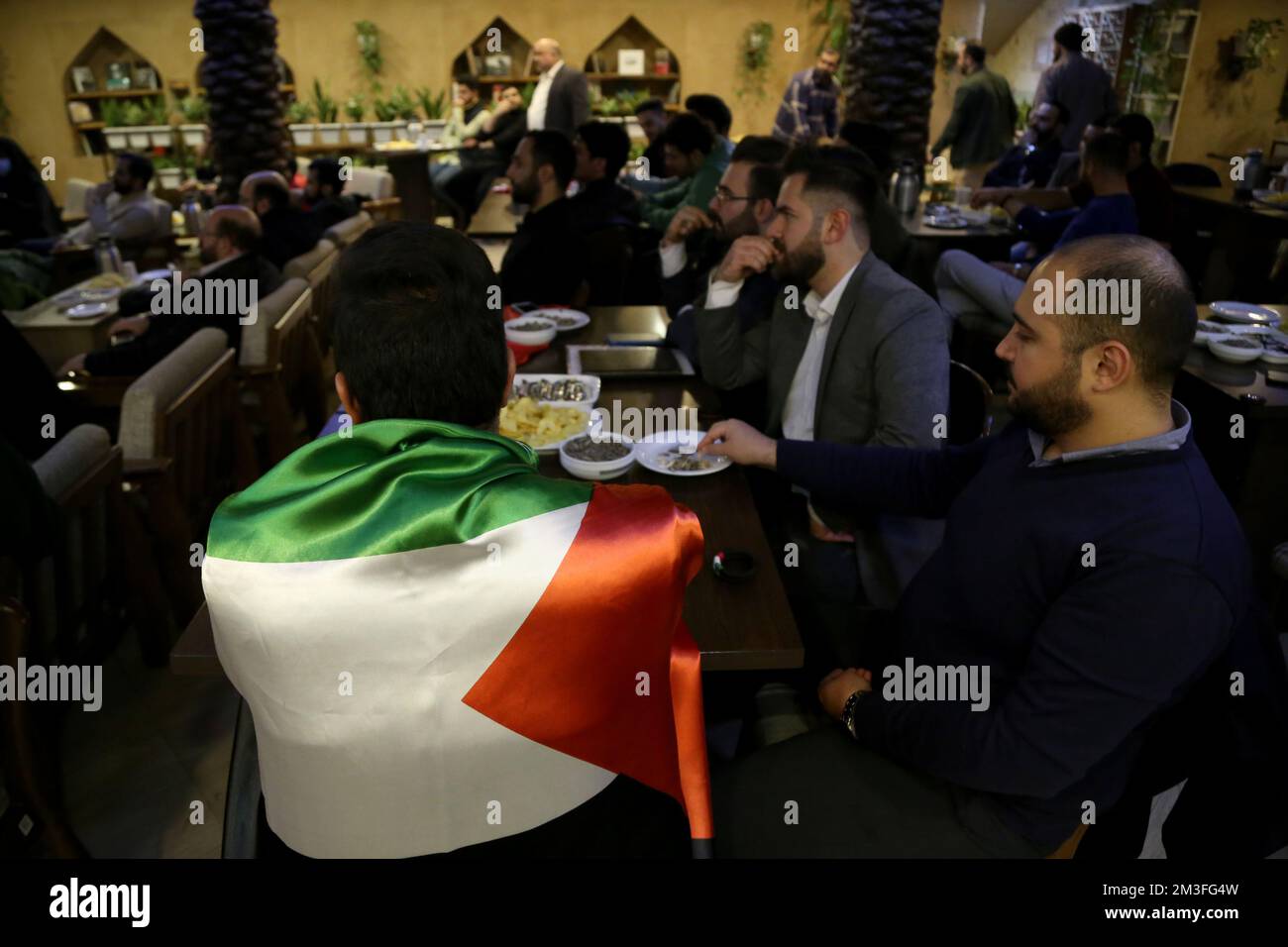 Téhéran, Téhéran, Iran. 14th décembre 2022. Un fan iranien portant un drapeau palestinien tout en assistant au café Nakhlestan dans le centre-ville de Téhéran pour avoir regardé la demi-finale du match de la coupe du monde de la FIFA, Qatar 2022 entre la France et le Maroc sur l'écran, 14 décembre 2022. Les fans d'Iran, du Liban, du Yémen, de Syrie et de Palestine se rassemblent au café de Nakhlestan, qui est géré et détenu par l'organisation artistique et médiatique Owj (IRGS) du corps des Gardiens de la révolution islamique, pour soutenir l'équipe nationale marocaine. Après la victoire contre le Portugal au Qatar sur 10 décembre, les Marocains ont porté des drapeaux palestiniens pour montrer leur suppo Banque D'Images