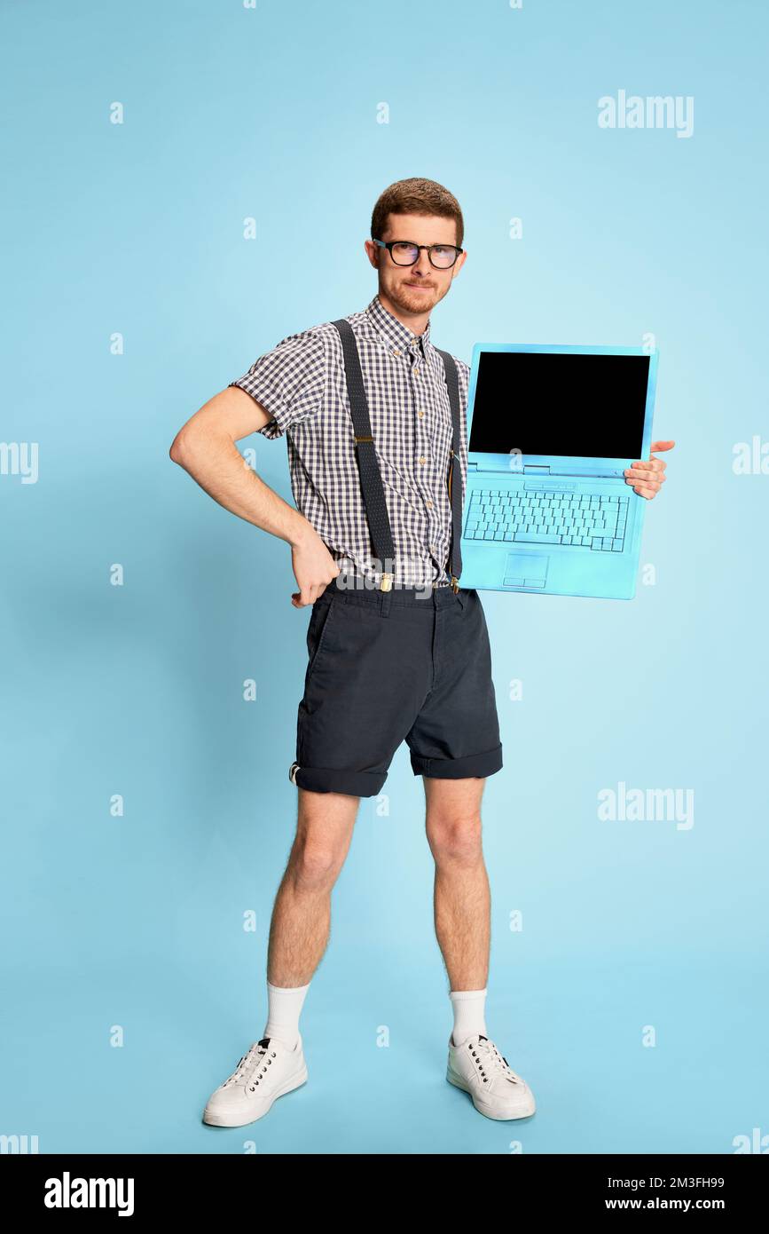 Jeune homme en chemise à carreaux, short et bretelles posant avec un  ordinateur portable isolé sur fond bleu. Des ventes importantes Photo Stock  - Alamy