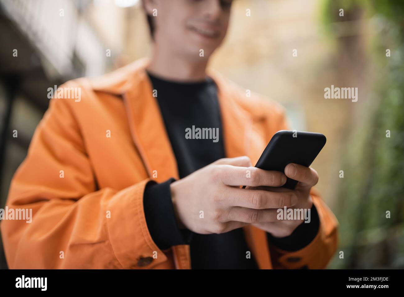 Vue rognée de l'homme flou dans la veste avec smartphone extérieur, image de stock Banque D'Images