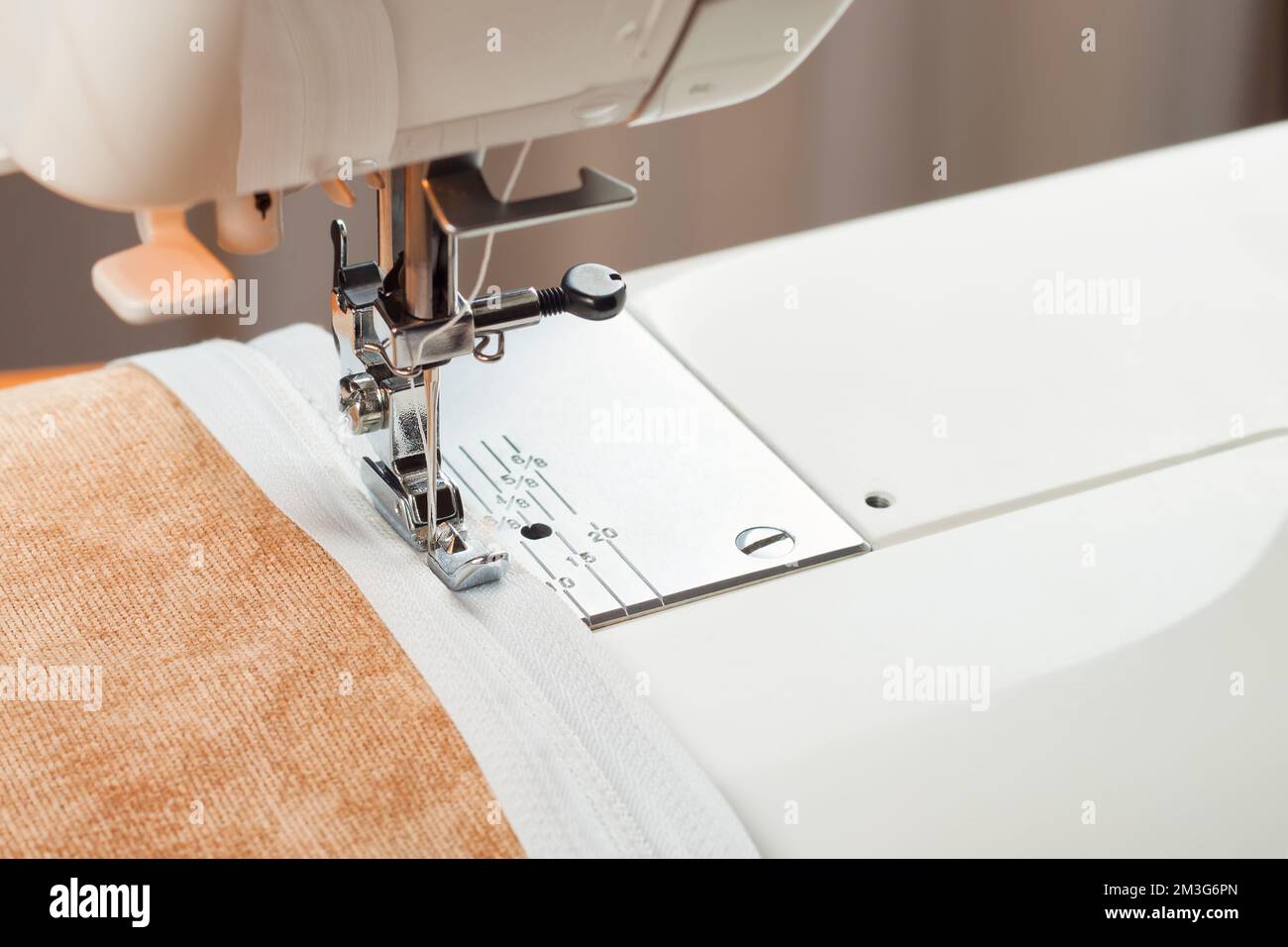 La machine à coudre moderne fait des coutures sur la fermeture éclair sur un vêtement beige. processus de couture Banque D'Images
