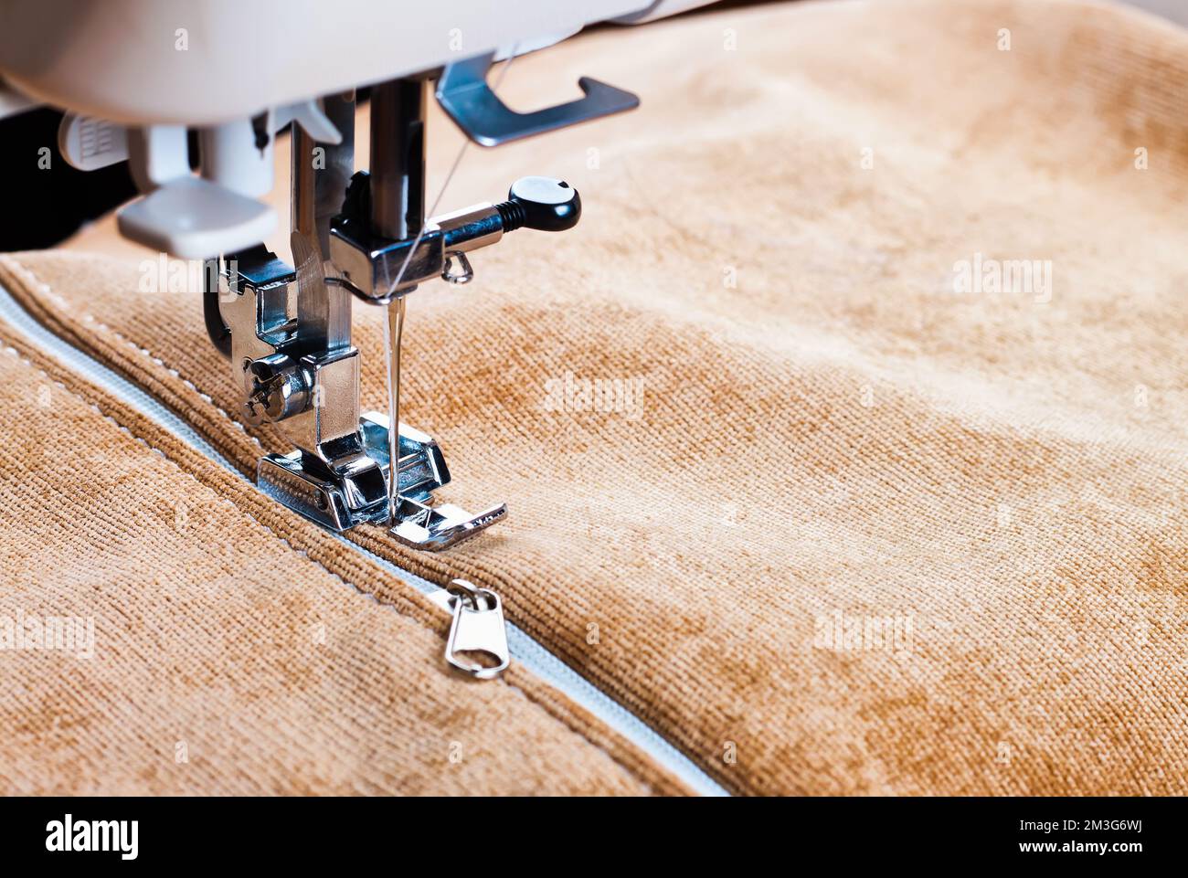 Machine à coudre moderne ragoûts sur la fermeture éclair sur biege article de vêtements. Processus de couture Banque D'Images