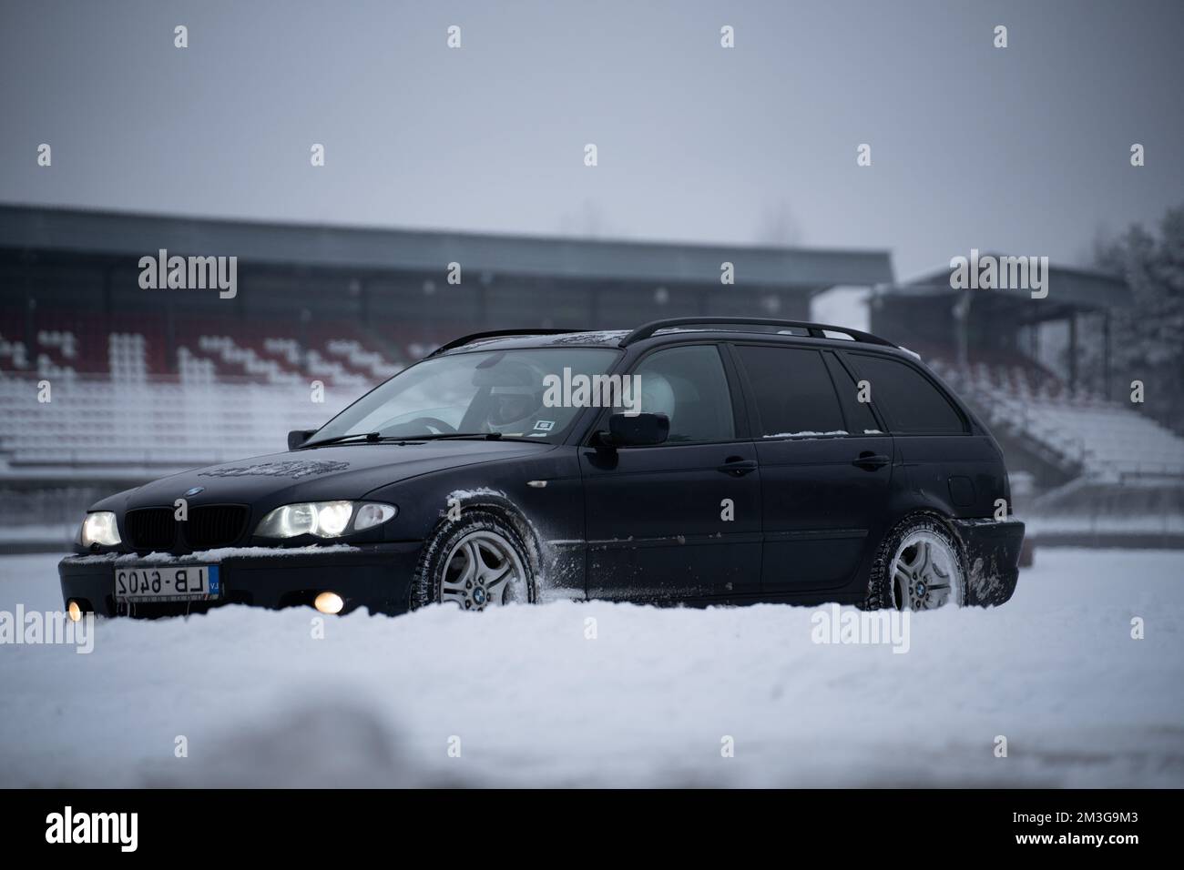 12-12-2022 Riga, Lettonie une voiture noire garée dans la neige près d'un stade avec un bâtiment en arrière-plan et un champ couvert de neige. . Banque D'Images