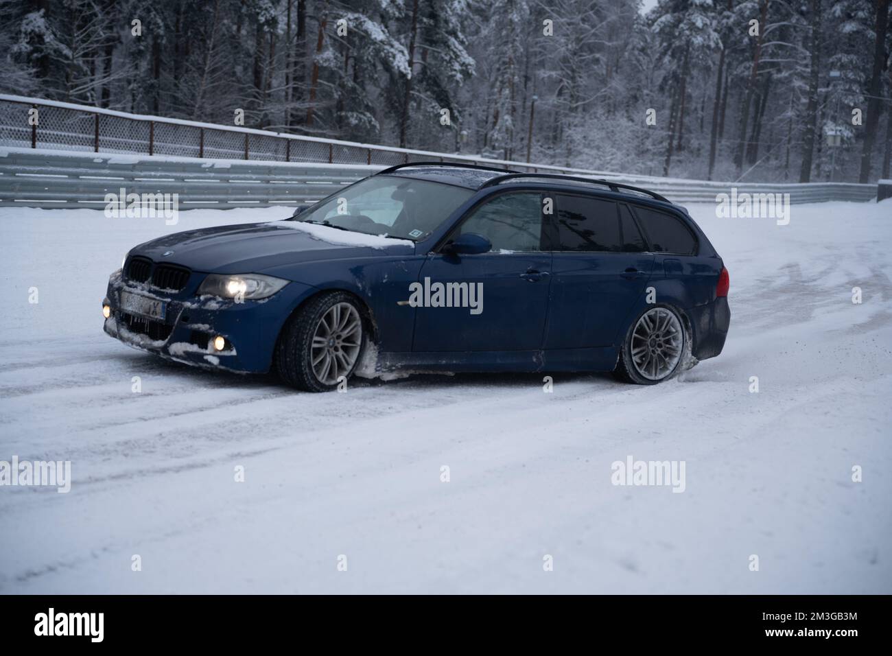 12-12-2022 Riga, Lettonie une voiture bleue est garée dans la neige près d'une clôture et d'arbres en arrière-plan. . Banque D'Images