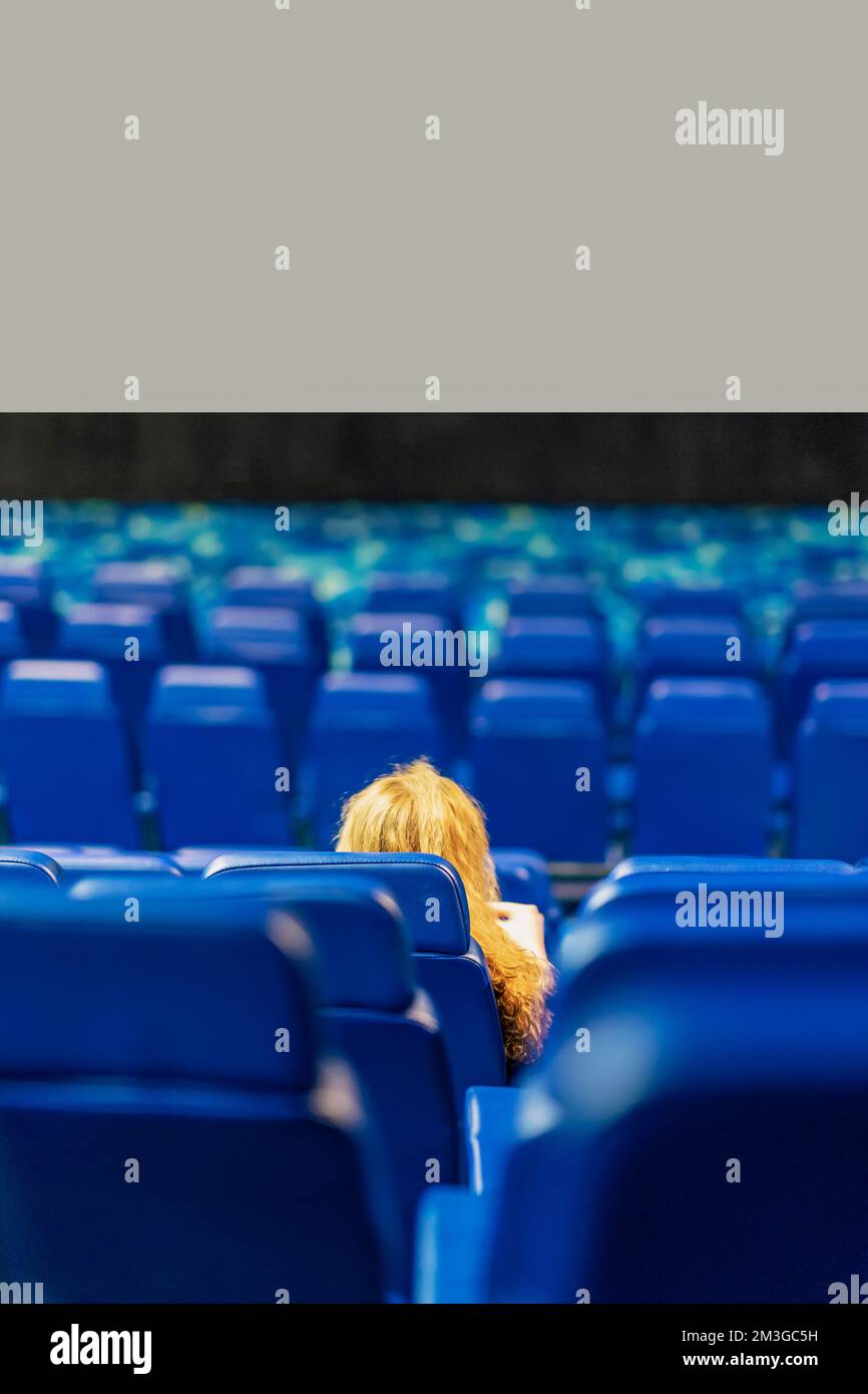 Vue arrière sur une petite fille abstraite assise dans une salle de cinéma vide, arrière-plan flou Banque D'Images
