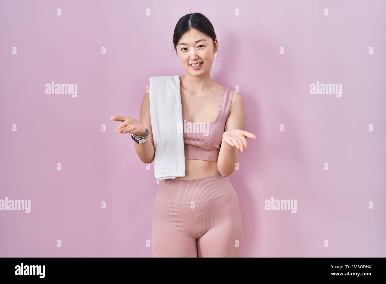 Jeune femme chinoise portant des vêtements de sport et une serviette souriante offrant des mains souriantes donnant assistance et acceptation. Banque D'Images