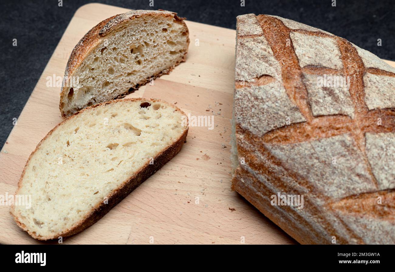 Pain ovale de levain fraîchement cuit couteau à pain sur planche à découper en bois, vue en angle. Pain rustique au levain sur table gris foncé Banque D'Images