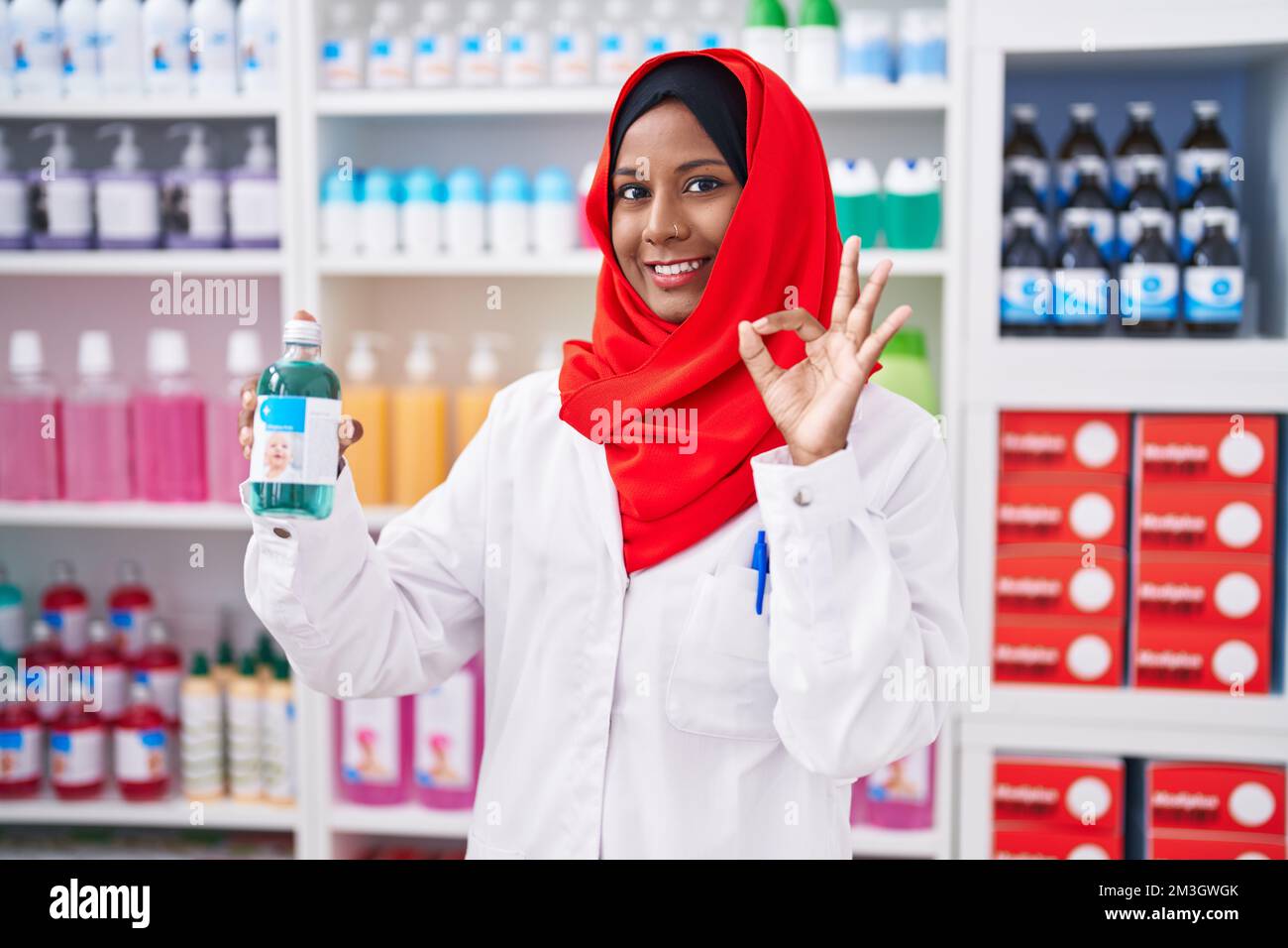Jeune femme arabe travaillant à pharmacie pharmacie pharmacie pharmacie pharmacie pharmacie tenue sirop faisant signe ok avec les doigts, souriant sympathique gestante excellent symbole Banque D'Images