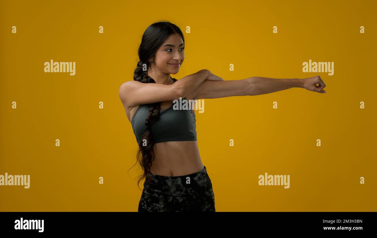 Femme multiraciale indienne sportive fille entraîneur sportif athlète sportive femme dans jaune studio parler regardant à l'appareil-photo expliquer l'exercice montrant main bras et Banque D'Images