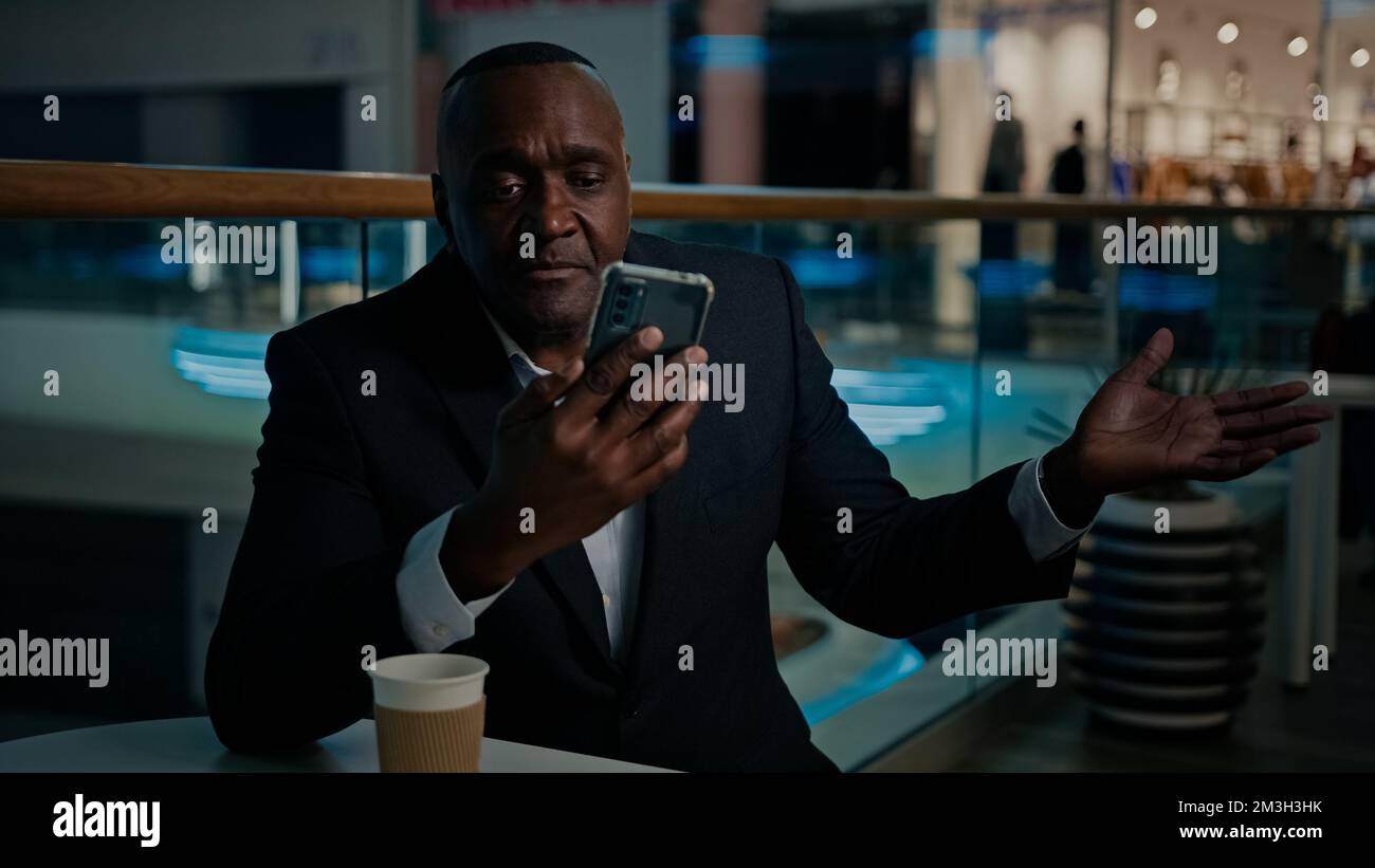 Ethnique Africain américain homme employeur entrepreneur dans le café avec thé parler appel vidéo d'affaires avec téléphone mobile conférence téléphonique Banque D'Images