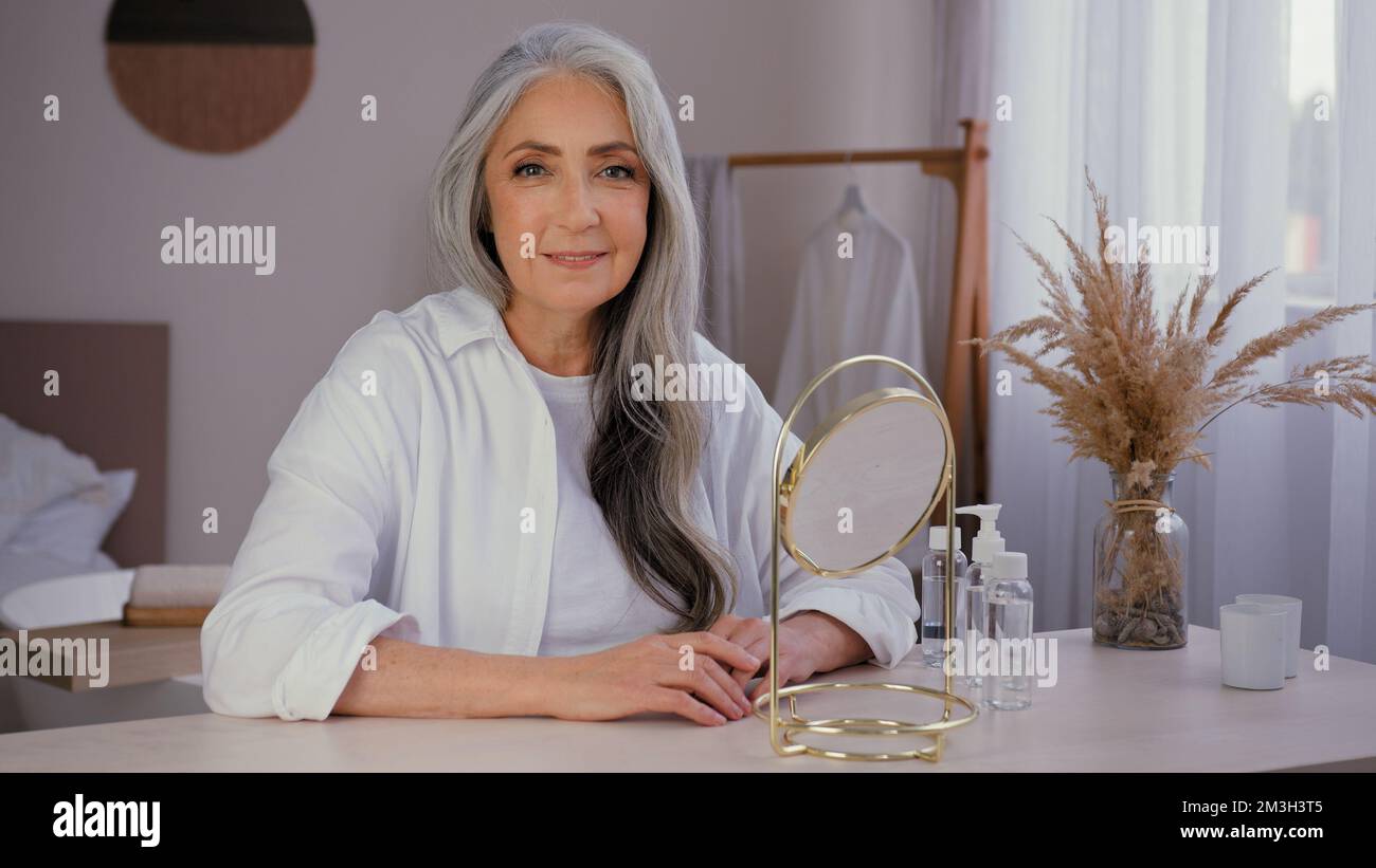 Vieille femme caucasienne souriante 60s femme sourire senior femme mûre avec miroir à la maison regardant la caméra grand-mère modèle 50s appréciez la peau du visage rides Banque D'Images