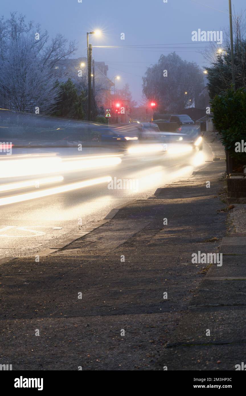 Circulation en banlieue : en hiver, les voitures descendent une pente douce, les phares se flent sous les lampadaires éclairés et les feux de circulation s'allument Banque D'Images