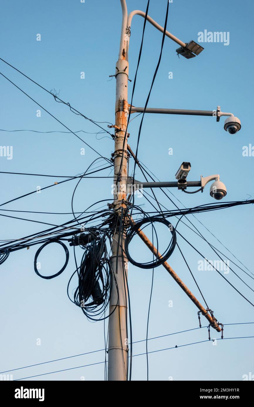 Poteau de câble d'électricité désordonné, ciel bleu en arrière-plan. Réseau électrique haute tension, dangereusement emmêlé. Banque D'Images