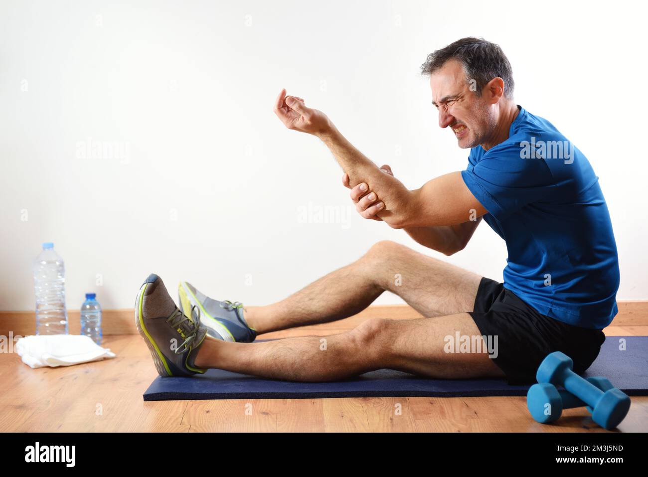 Homme faisant du sport à l'intérieur se plaignant de douleurs d'avant-bras assis sur un tapis. Vue latérale Banque D'Images