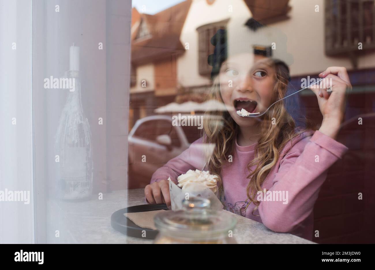 fille buvant du chocolat chaud et mangeant du gâteau dans un siège de fenêtre de café Banque D'Images