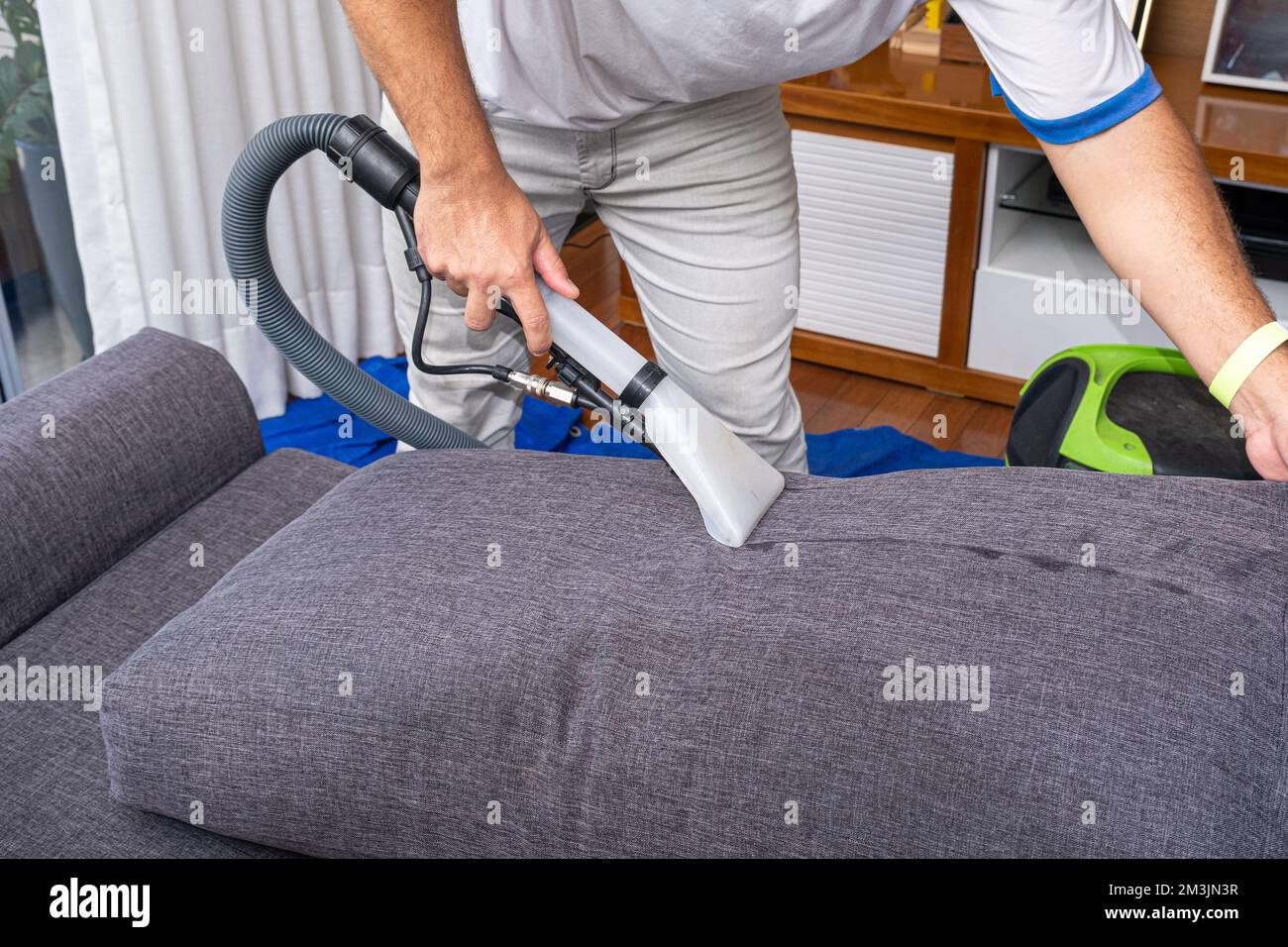 Homme utilisant un aspirateur spécial pour nettoyer les coussins gris du canapé vue latérale. Banque D'Images