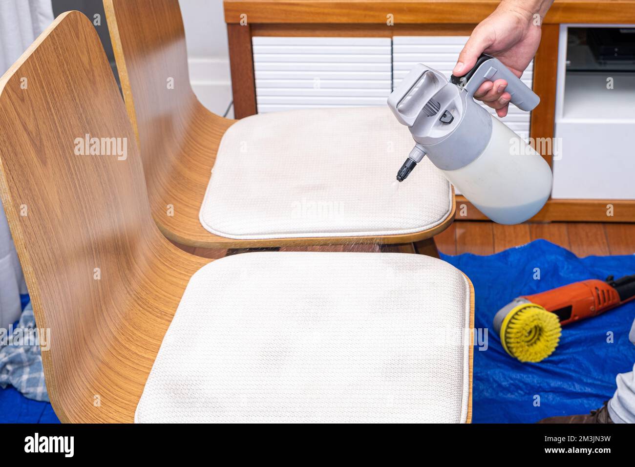 Homme pulvérisant du liquide de nettoyage sur le coussin de chaise. Banque D'Images