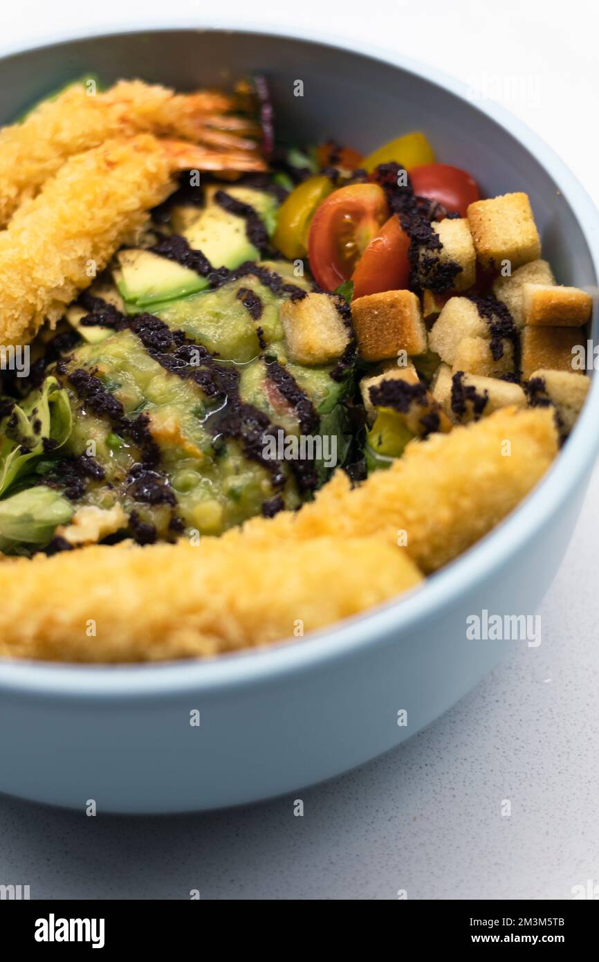 Poisson pané sur un bol bleu de poke de légumes avec avocat sur un brunch sain et savoureux toujours en gros plan Banque D'Images