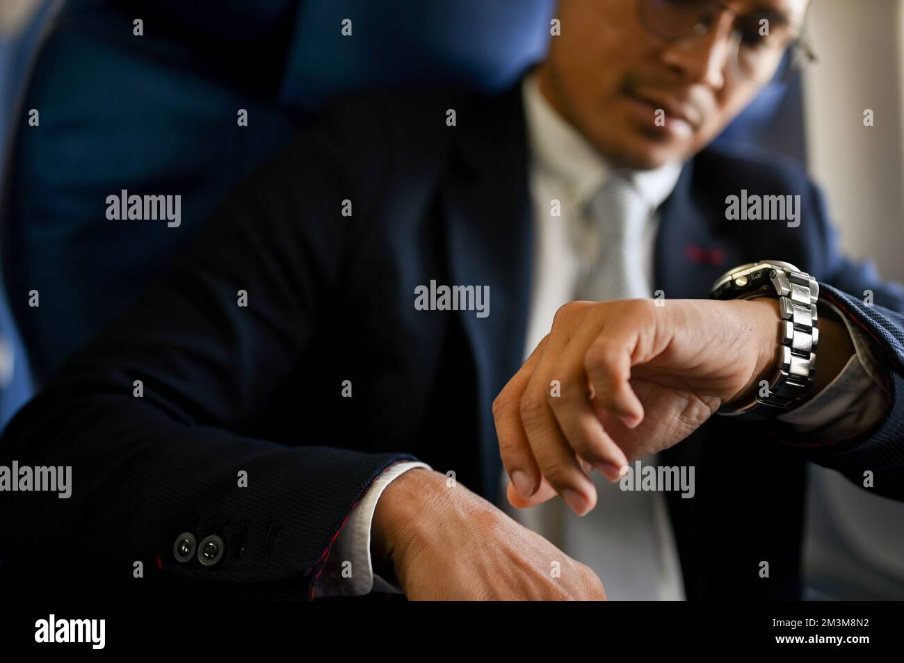 Gros plan, homme d'affaires asiatique professionnel et prospère qui vérifie l'heure d'arrivée de sa montre. jet privé, vol privé. Banque D'Images