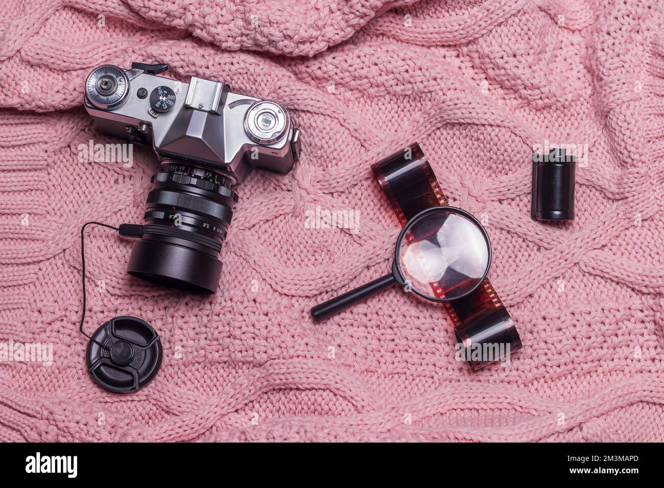 Un ancien appareil photo rétro, un film photographique et une loupe se trouvent sur un pull en laine rose. Banque D'Images