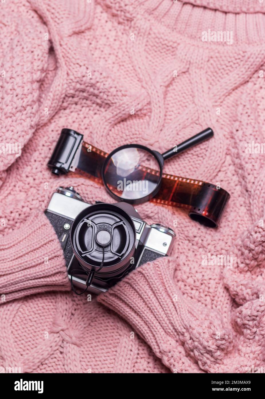 Un ancien appareil photo rétro avec un objectif fermé repose sur un pull en laine rose. Banque D'Images