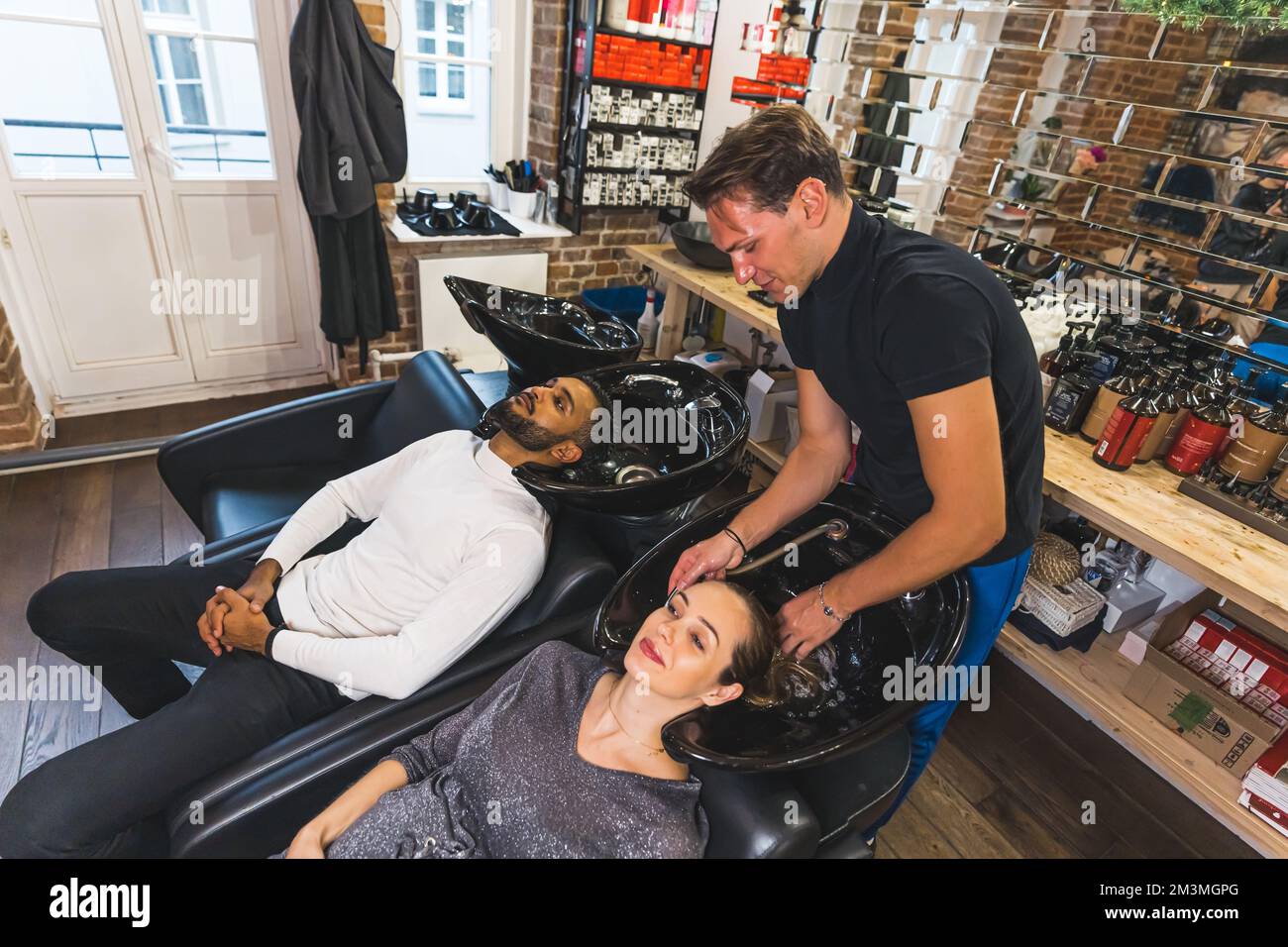 Coiffeur professionnel souriant lavant les cheveux de ses clients masculins et féminins dans un salon de coiffure professionnel. Photo de haute qualité Banque D'Images